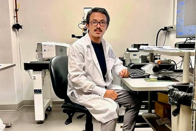 Mingmar Sherpa wears a lab coat and sits at a computer
