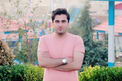 Hilal Mohammadzai stands with trees and houses in the background.