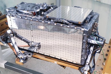 A closeup of one of the Laboratory-built payloads. The payload is silver in color and rectangular box-shaped with a few protrusions on the sides.