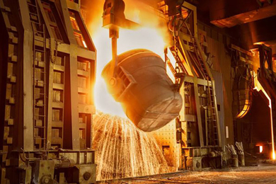 A large bucket pours molten steel in a heavy industrial setting