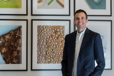 John Hart poses in front of some framed photomicrograph art