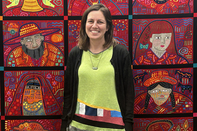 Daniela Giardina stands against a colorful quilted tapestry of different faces