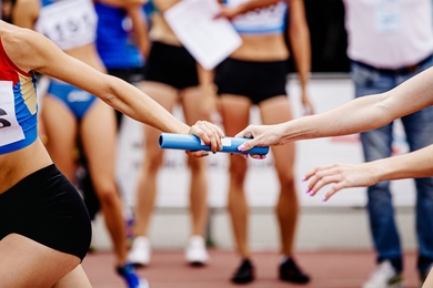 A closeup on the handoff of a blue baton between two runners in a relay race