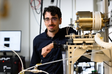 Marco Graffiedi in a lab with a computer screen in the background to the left and bronze colored instruments on a platform to the right.