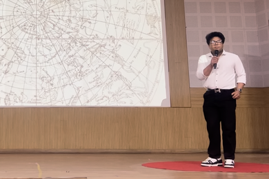 Vivan Mirchandani speaks in front of a screen, which shows graphics of constellations.