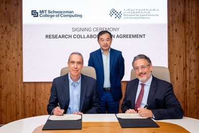 Dan Huttenlocher and Sami Haddadin, seated at a table, sign an agreement, with Eric Xing standing behind them
