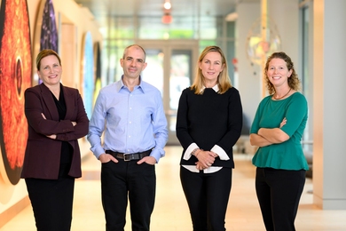 Angela Koehler, Iain Cheeseman, Katharina Ribbeck, and Caroline Lowenthal pose in a hall with brightly colored scientific art