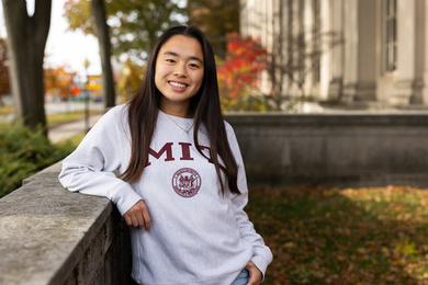 Sean Luk leans on stone wall on MIT campus