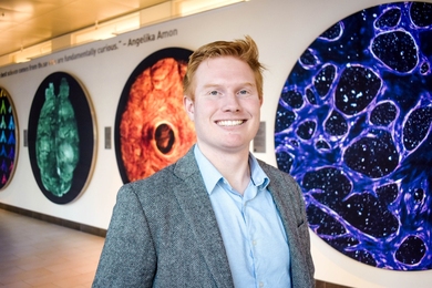 Matthew Jones poses in the Koch Institute Gallery with large scientific images behind him