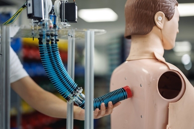 A human hand guides a cylindrical robot arm to touch a mannequin’s back