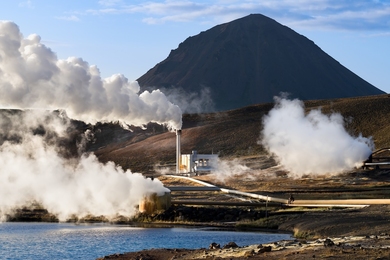 Photo of modest-sized power plant on treeless plain emiting steam clouds, with mountain in background