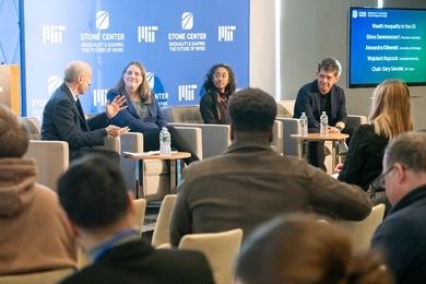 Gary Gensler, Alexandra Killewald, Ellora Derenoncourt, and Wojciech Kopczuk sit in armchairs onstage in front of a blue Stone Center banner