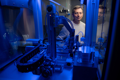 Joey Davis peers through a small blue-lit machine with a robot arm.