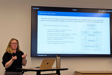 Emily Williams stands at a lectern with a laptop. Behind her is a slide that shows conclusions and outlooks learned from her research.